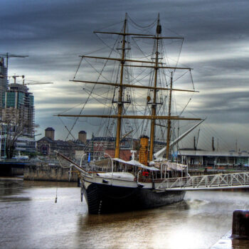 An image of a sailboat at a dock. The weather is cloudy and the water is calm.