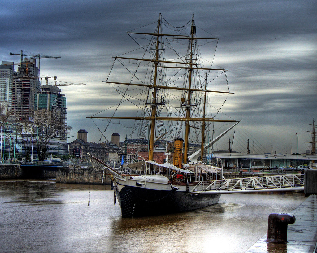 An image of a sailboat at a dock. The weather is cloudy and the water is calm.