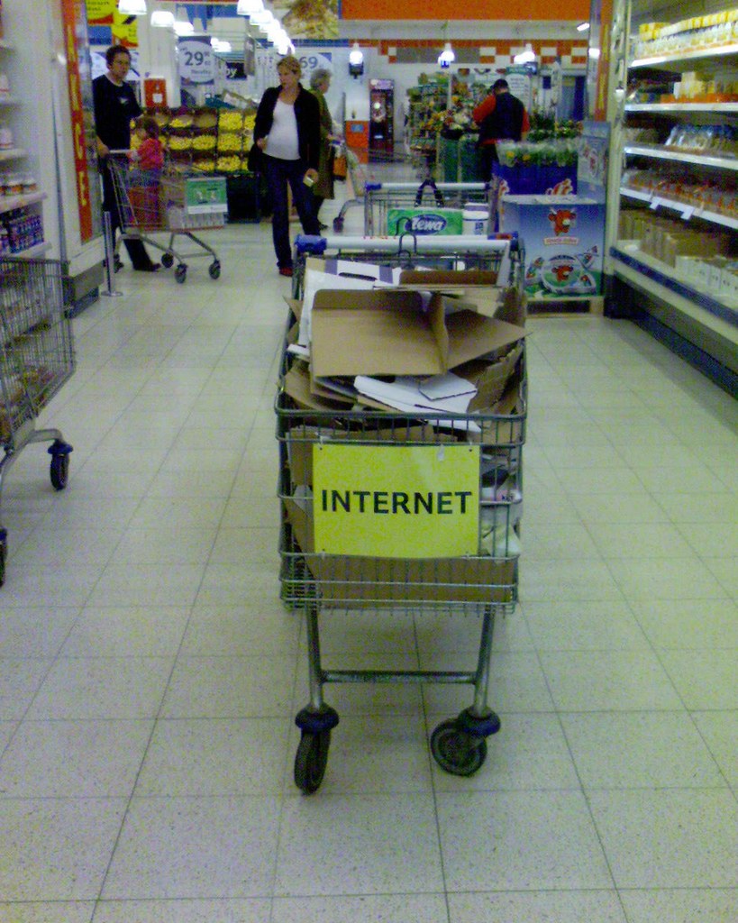 an image of a shopping cart full of scrap paper, cardboard, and other pieces of trash. A yellow piece of paper is on the front with the word "internet" in all caps.